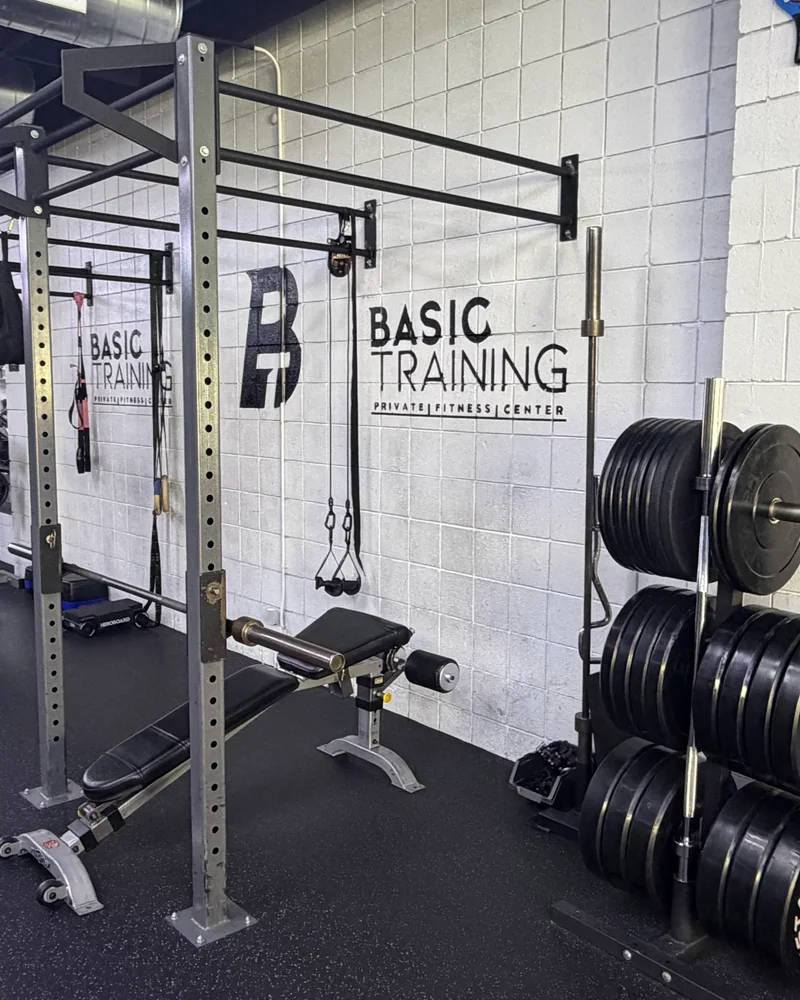 Wall-mounted squat and pull-up rig with barbells, bumper plates and an adjustable bench at BASIC Training in Glendale